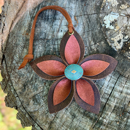 Leather flower-shaped keychain with a central turquoise element on a wooden surface