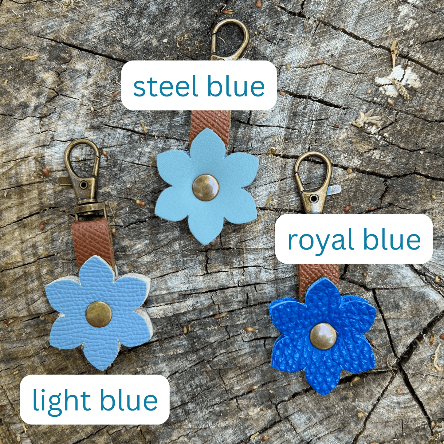 Three blue flower-shaped keychains on a wooden surface with labels for color.