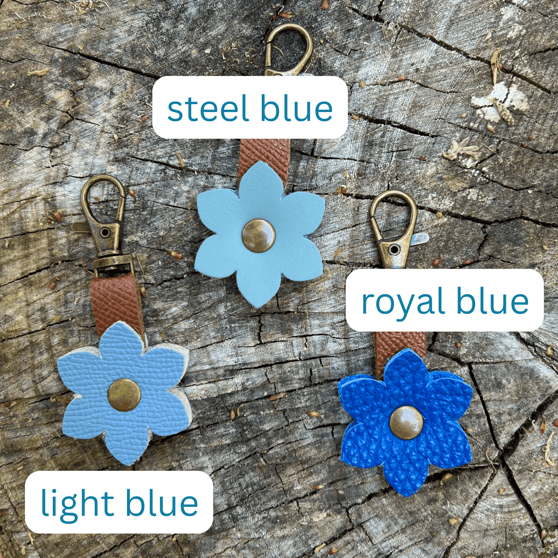 Three blue flower-shaped keychains on a wooden surface with labels for color.