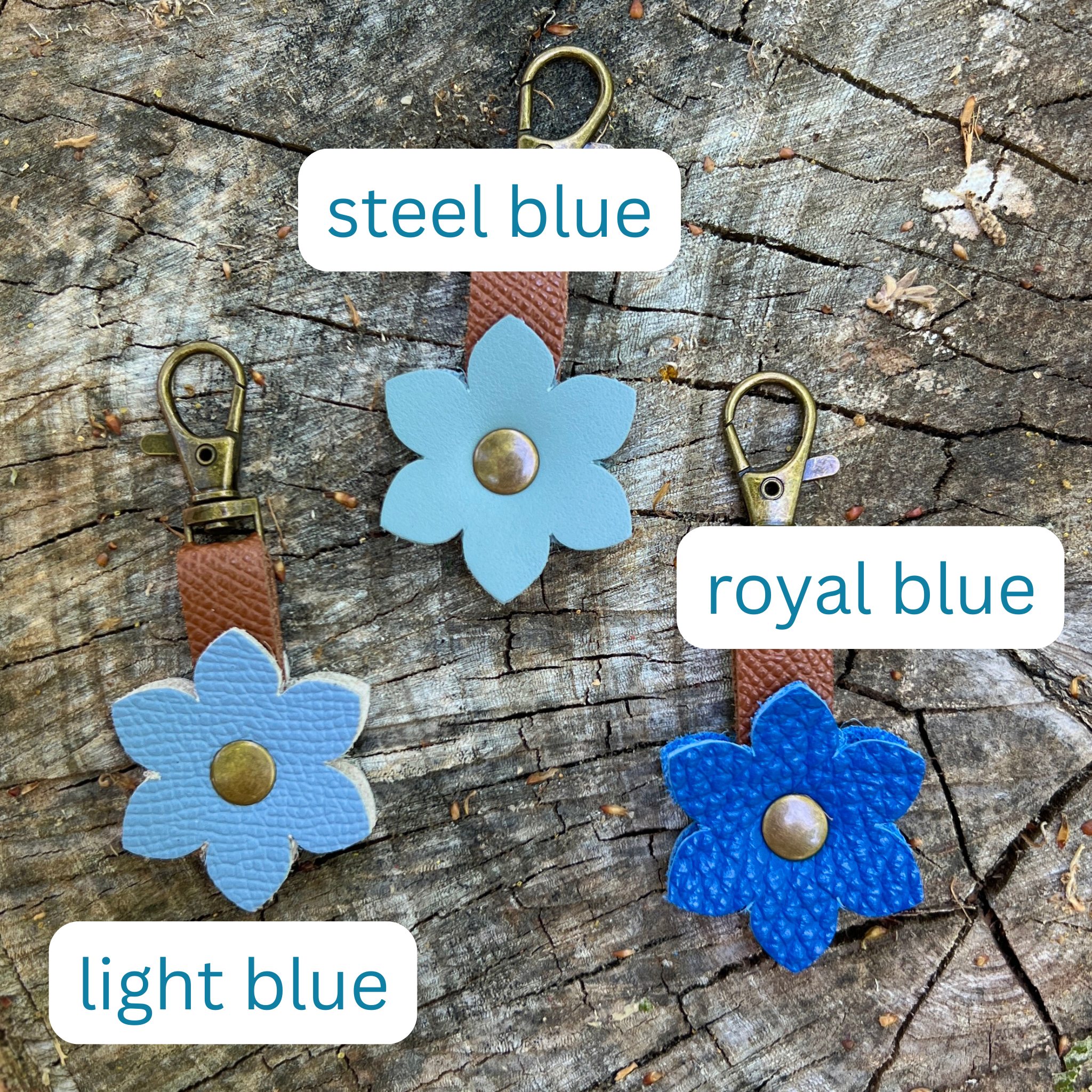 Three blue flower-shaped keychains on a wooden surface with labels for color.