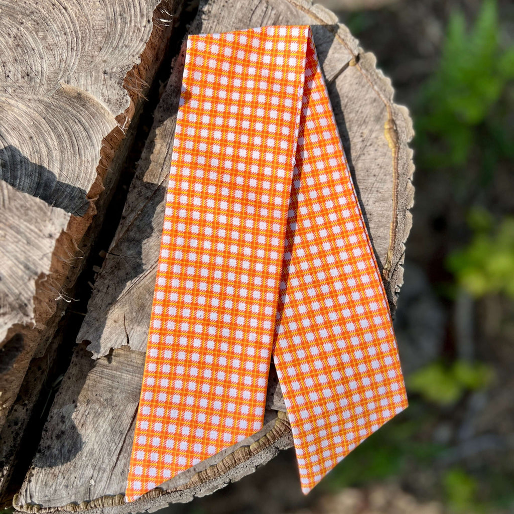purse scarf in Orange and white checkered fabric on a wooden log with blurred greenery in the background