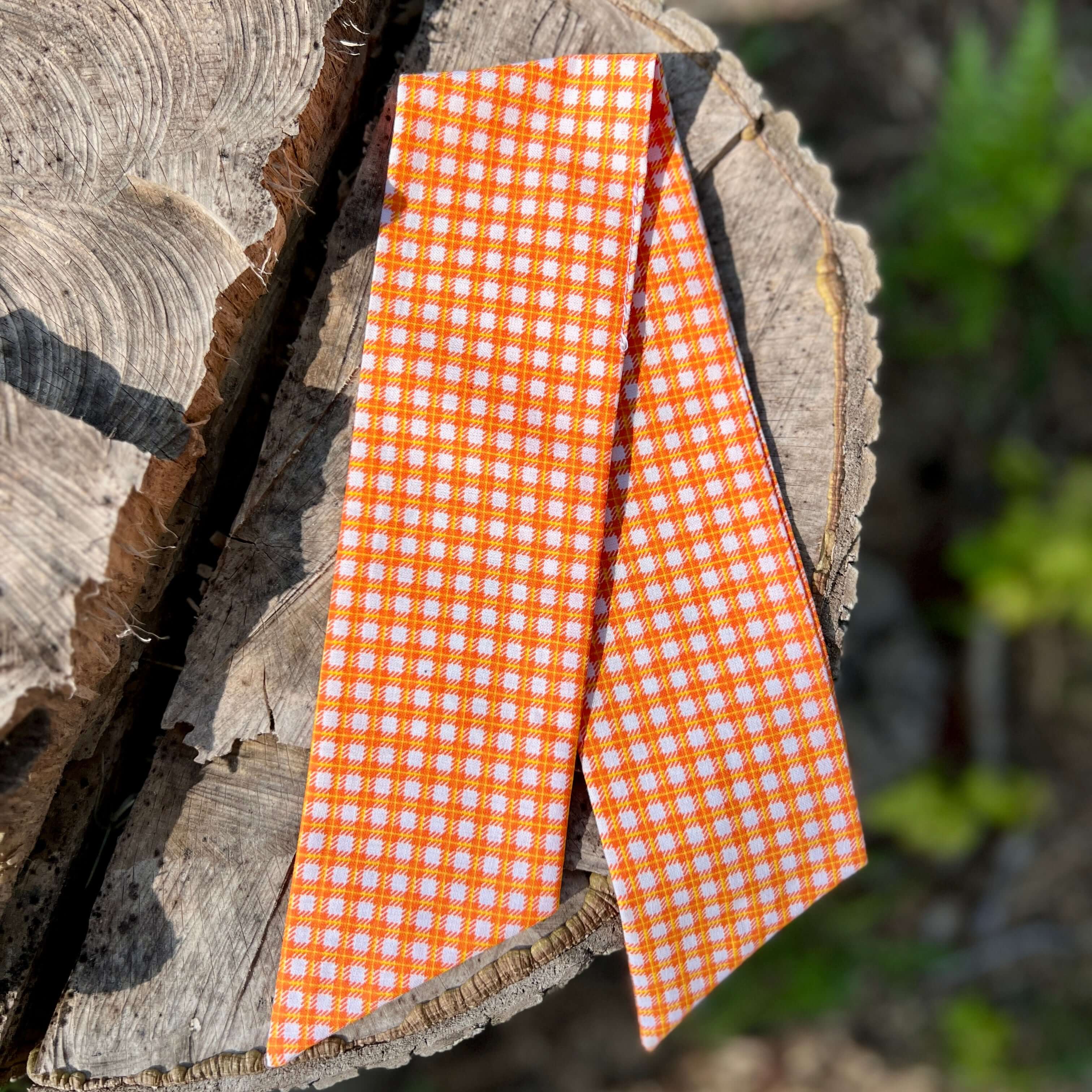 purse scarf in Orange and white checkered fabric on a wooden log with blurred greenery in the background