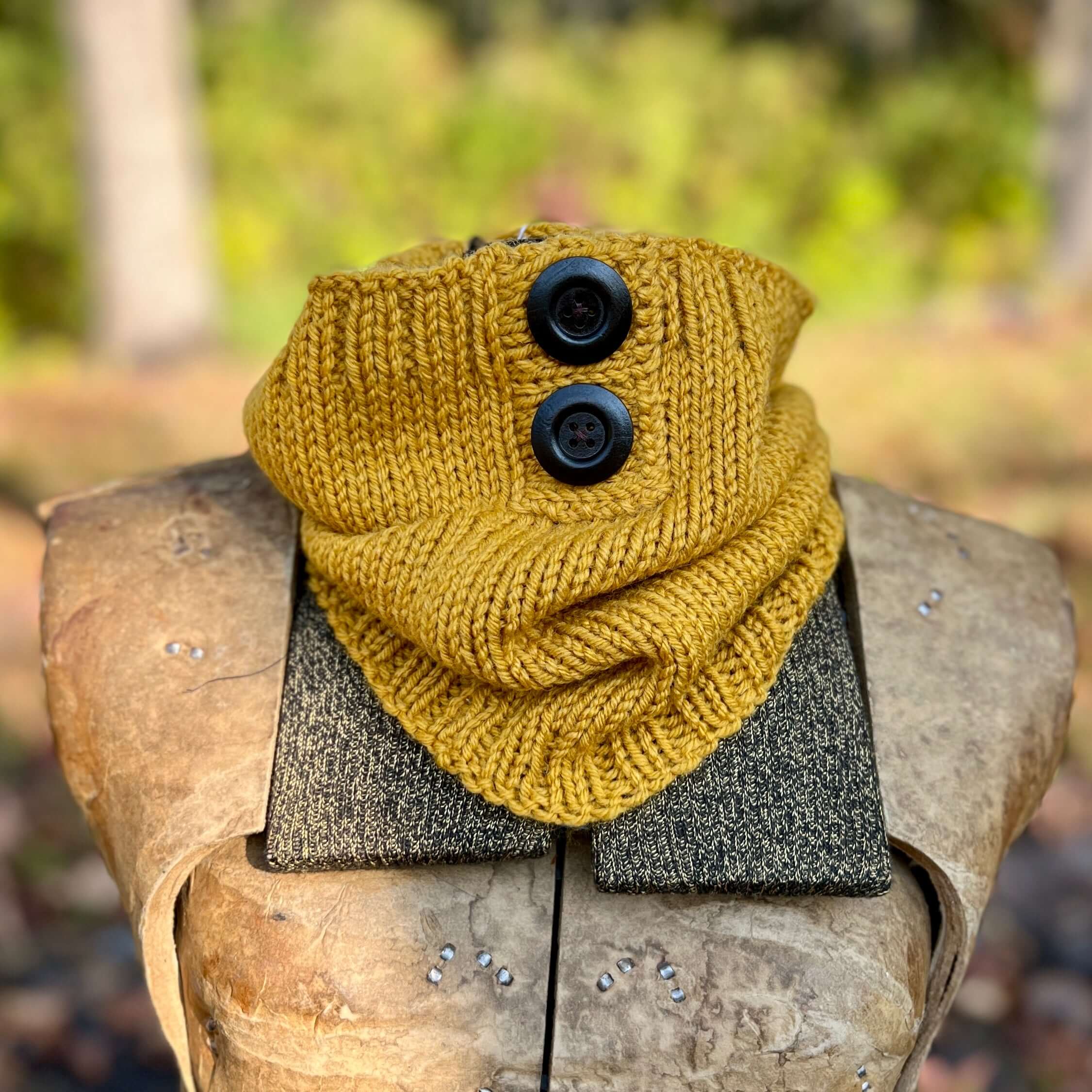 Yellow knitted scarf with black buttons on a wooden surface outdoors