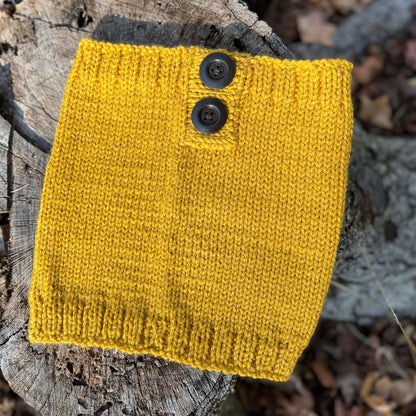 Yellow knitted scarf with two black buttons on a wooden surface