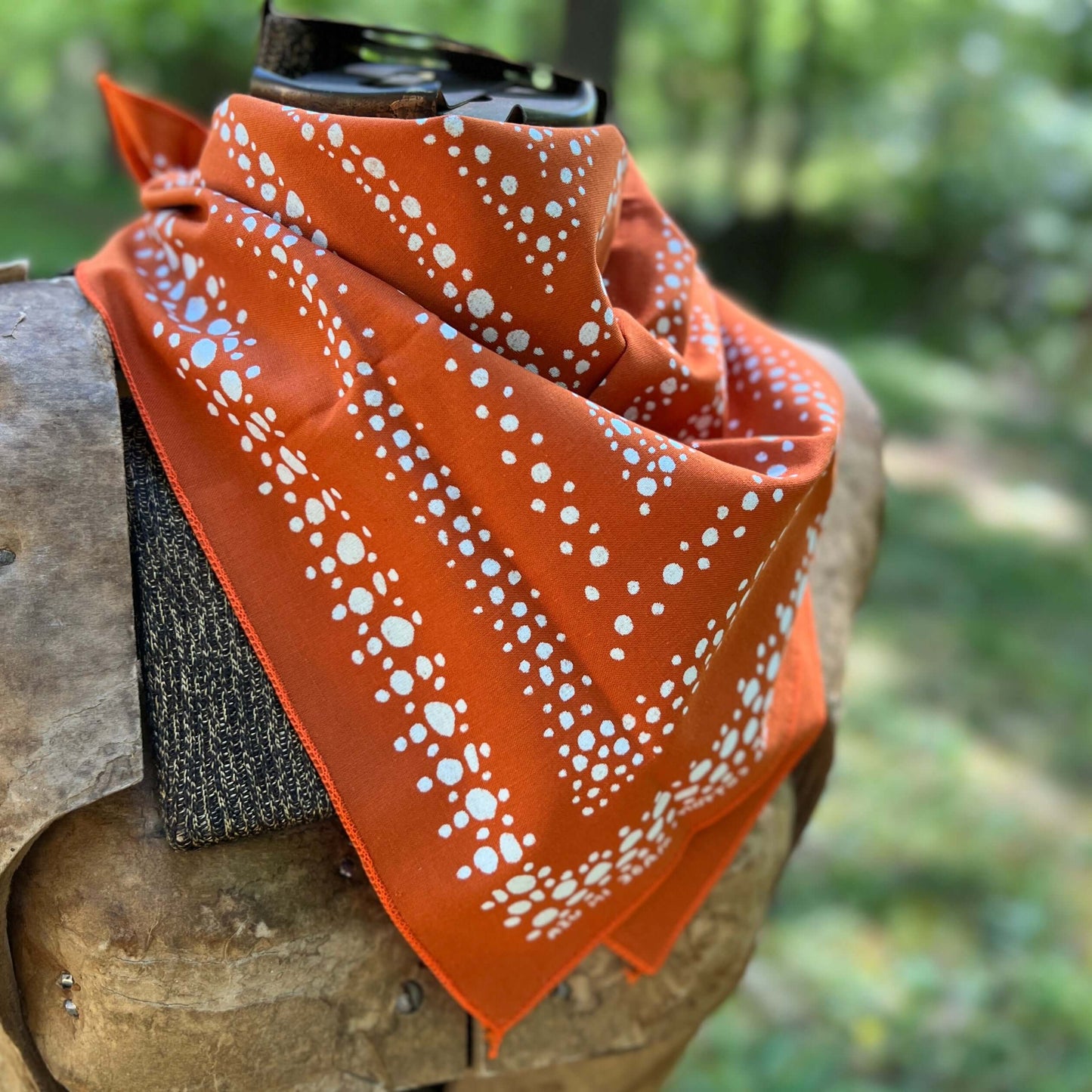 Orange bandana with white patterns draped over a wooden surface outdoors.