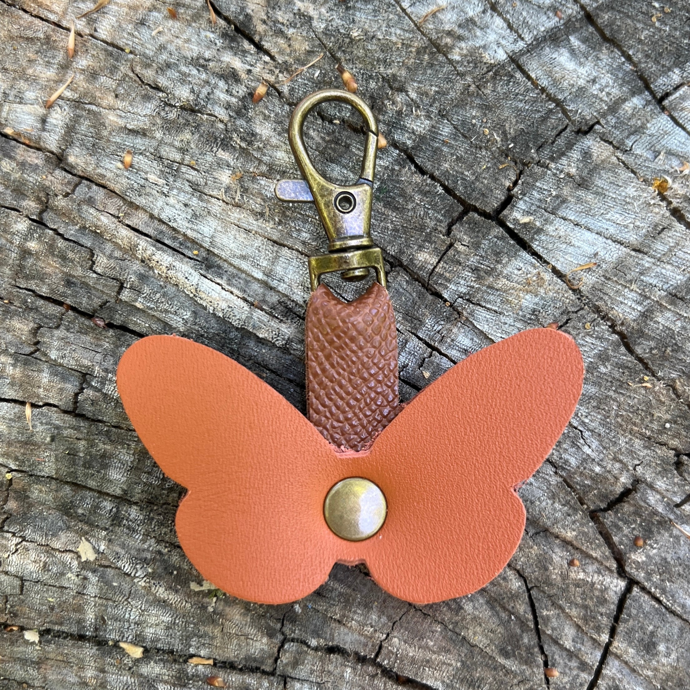 Butterfly-shaped keychain with a brown leather body and gold accents on a wooden surface