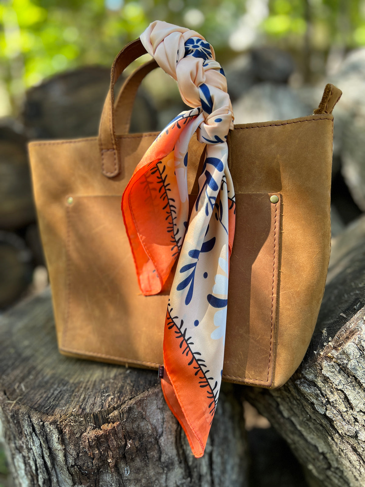 orange flower silky square scarf tied on handle of brown tote