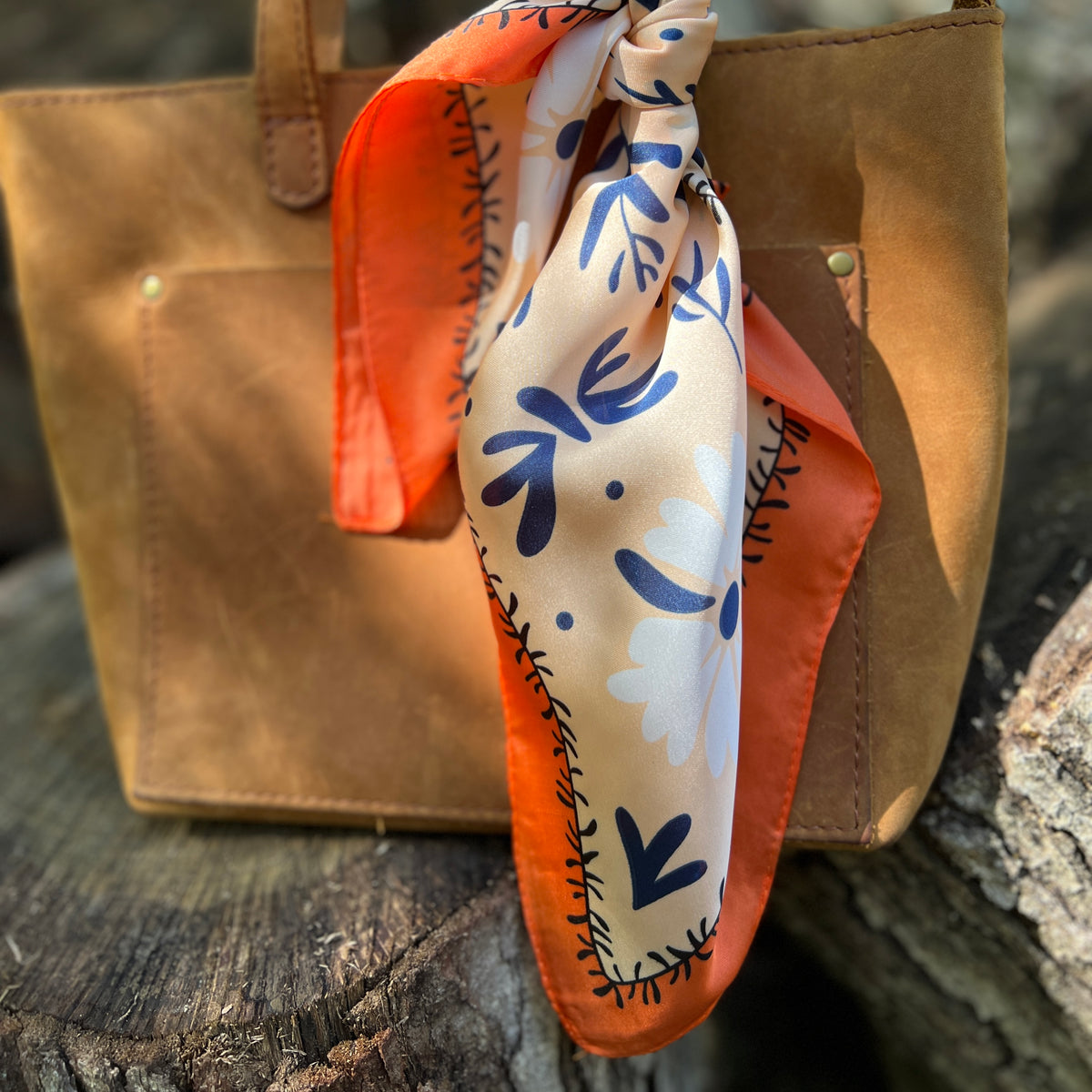 orange flower silky square scarf tied on handle of brown tote