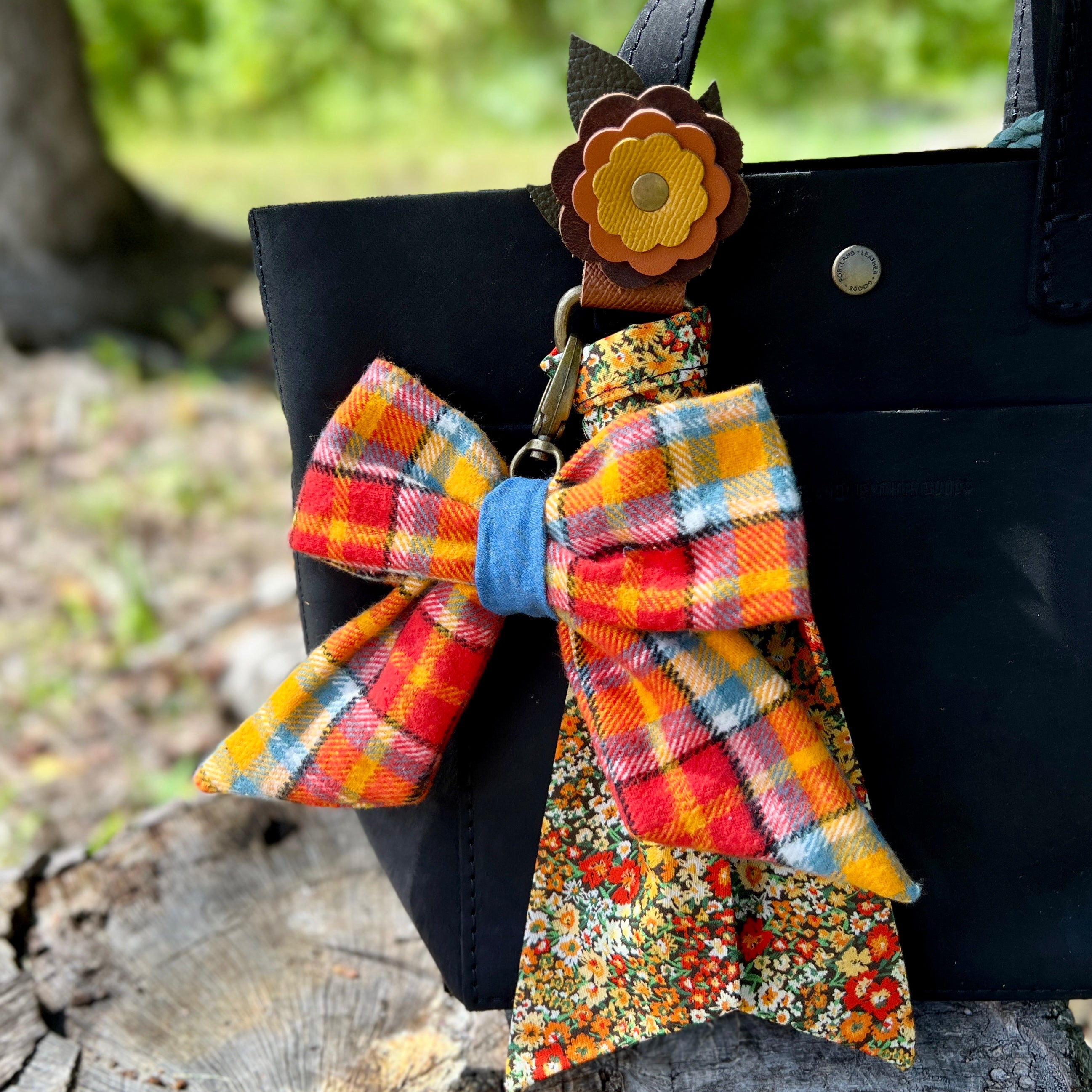Colorful plaid bow keychain attached to a black bag with a blurred natural background