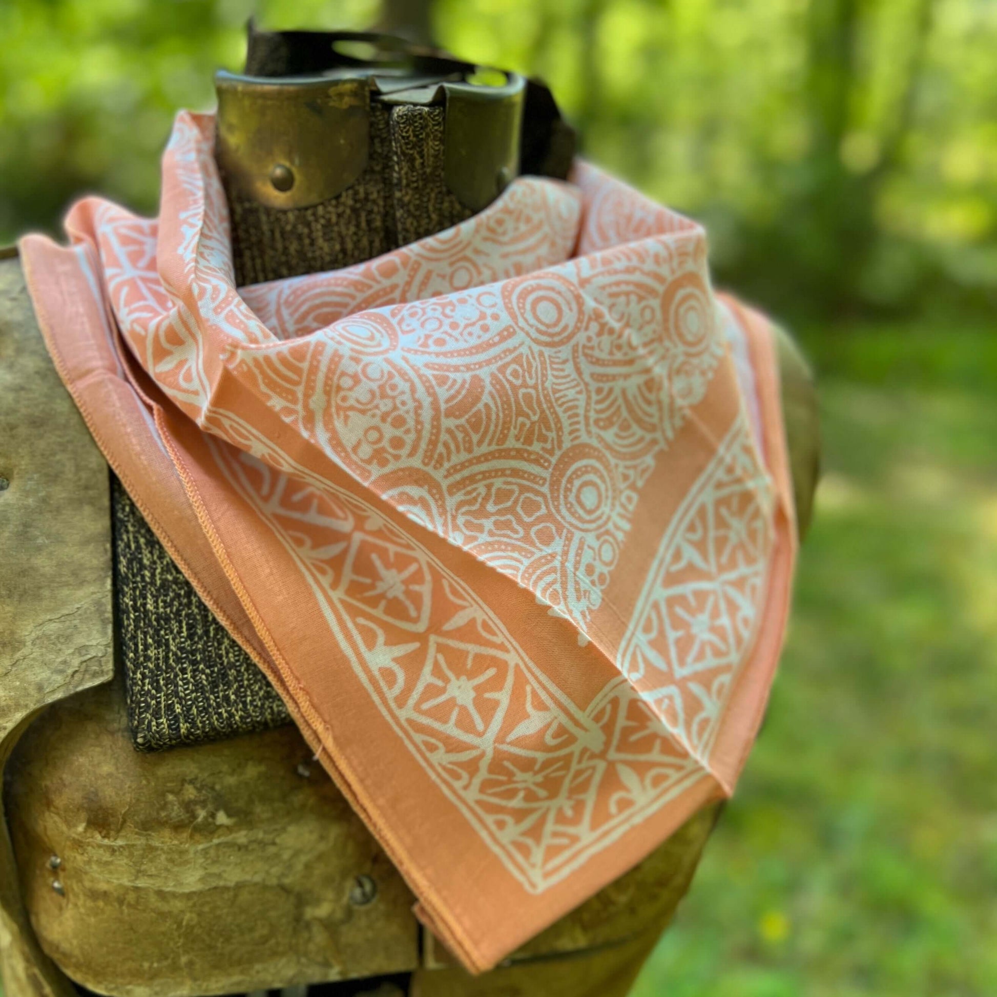 Peach-colored bandana with white patterns  against a blurred green background