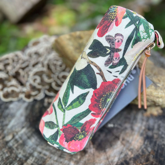 A fabric zippered pencil case with a colorful floral and butterfly print, resting on a rustic wooden surface with a lace doily in the background.