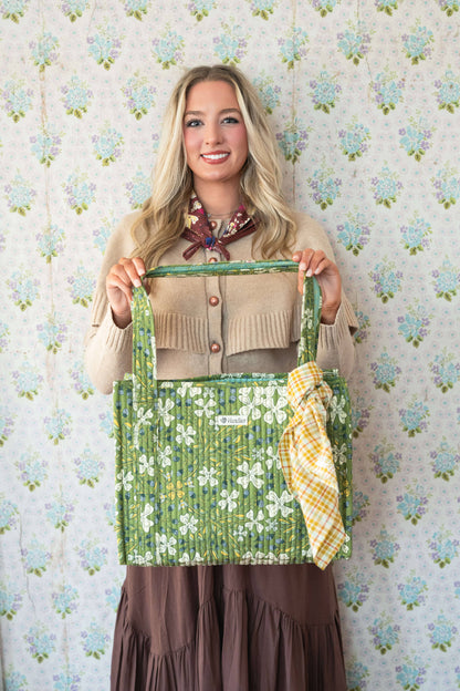 Woman holding a green floral-patterned bag against a floral wallpaper background