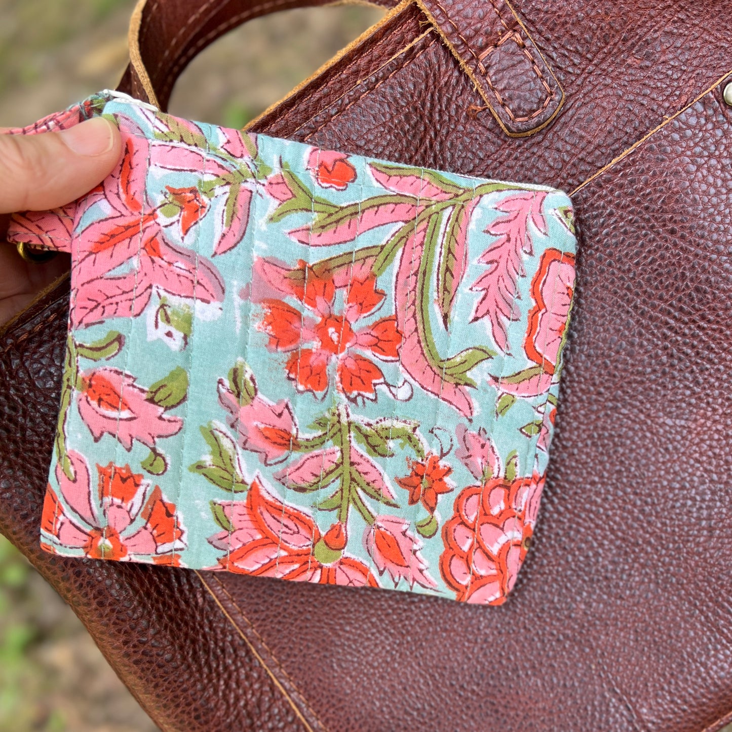 Floral patterned pouch held over a brown leather bag