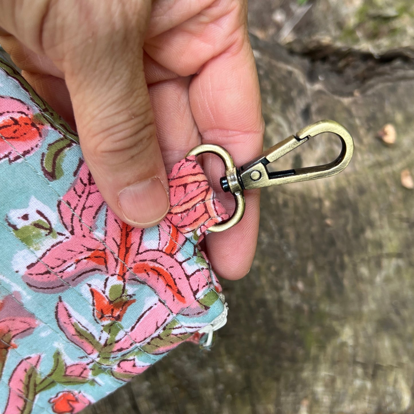 Hand holding a floral-patterned pouch with a brass keychain clip against a natural background.