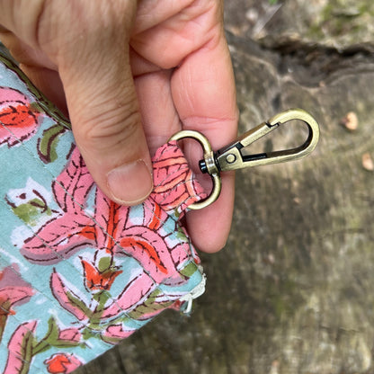 Hand holding a floral-patterned pouch with a brass keychain clip against a natural background.