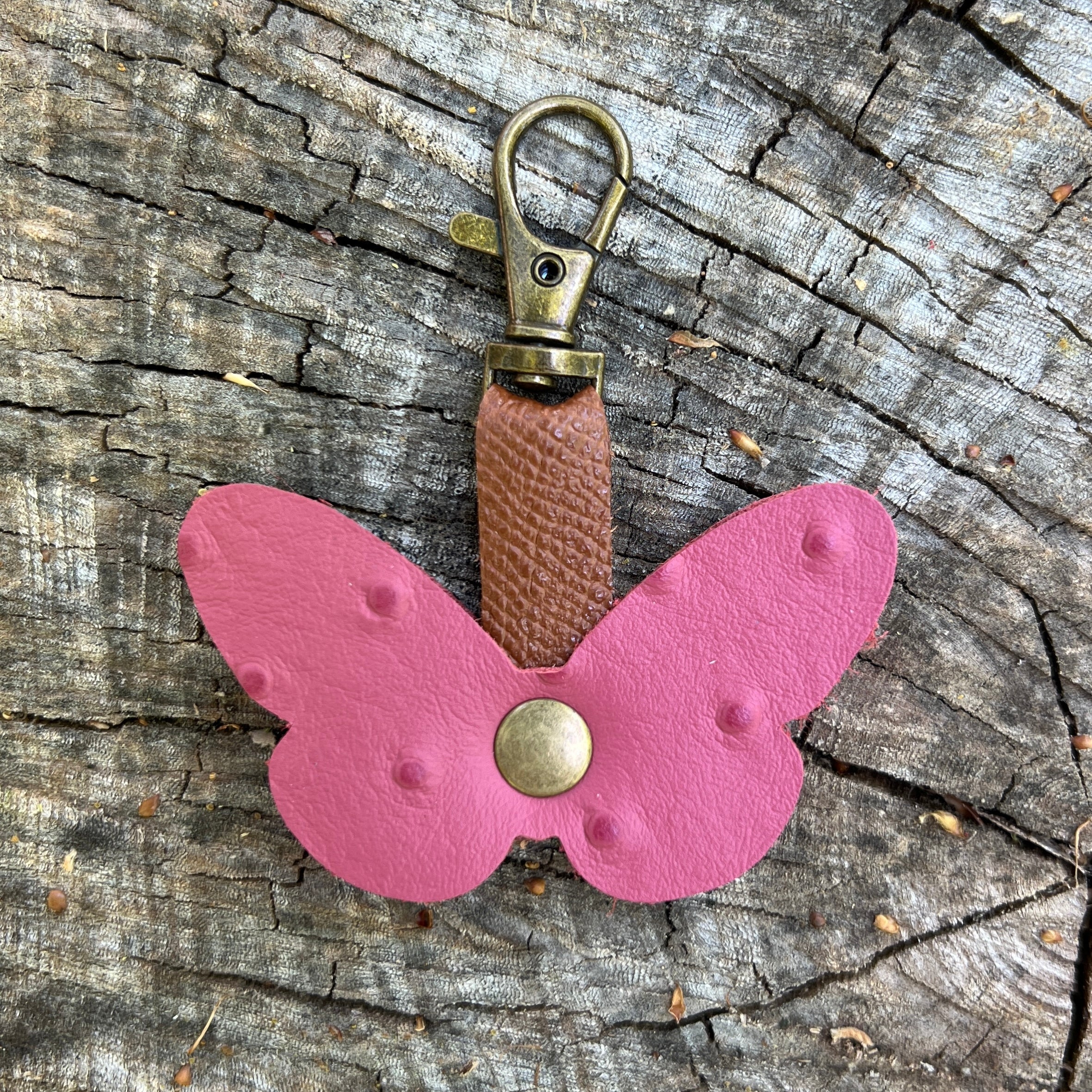 Pink butterfly keychain with a brown strap on a wooden surface