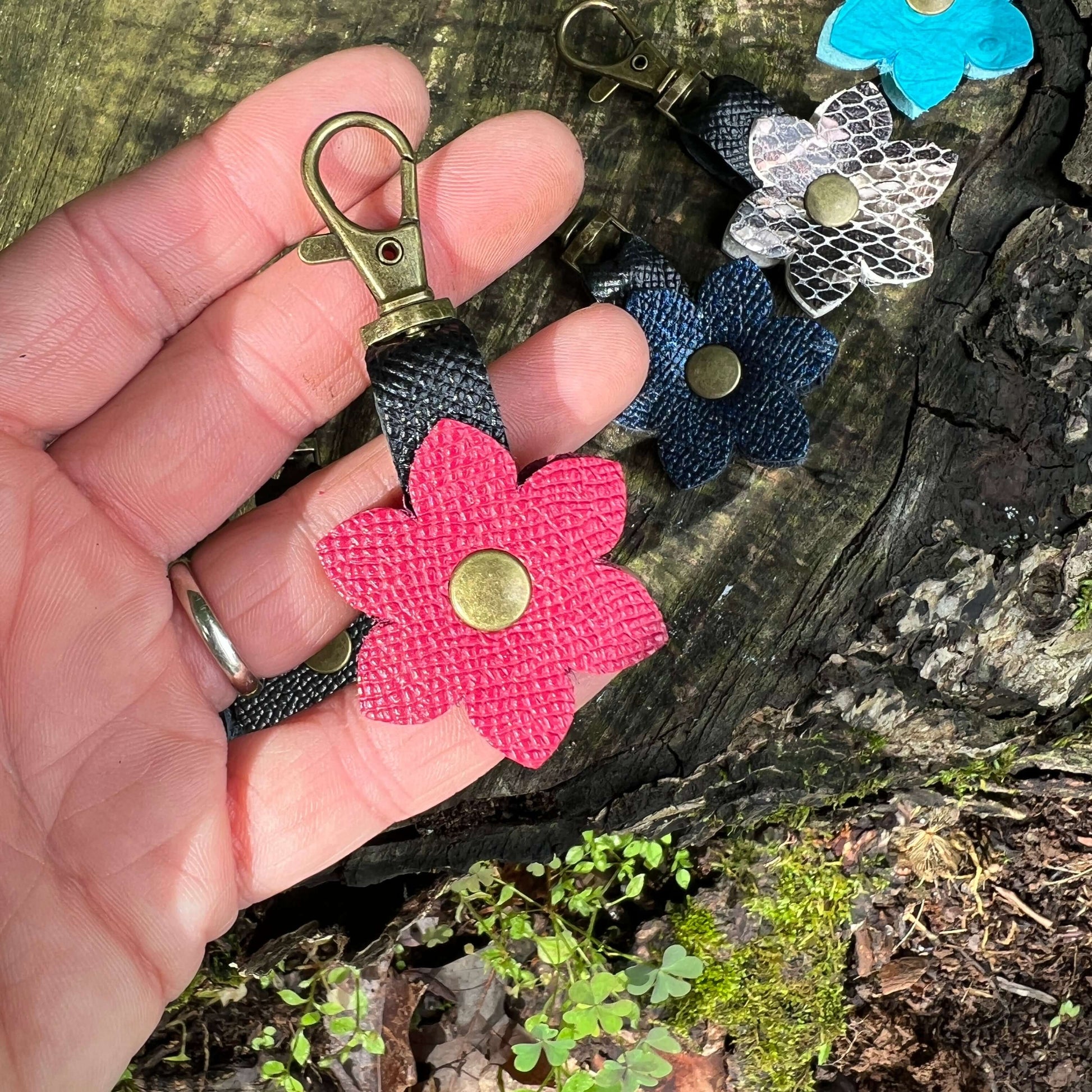 Hand holding a pink flower-shaped keychain with a metal clasp on a natural background.