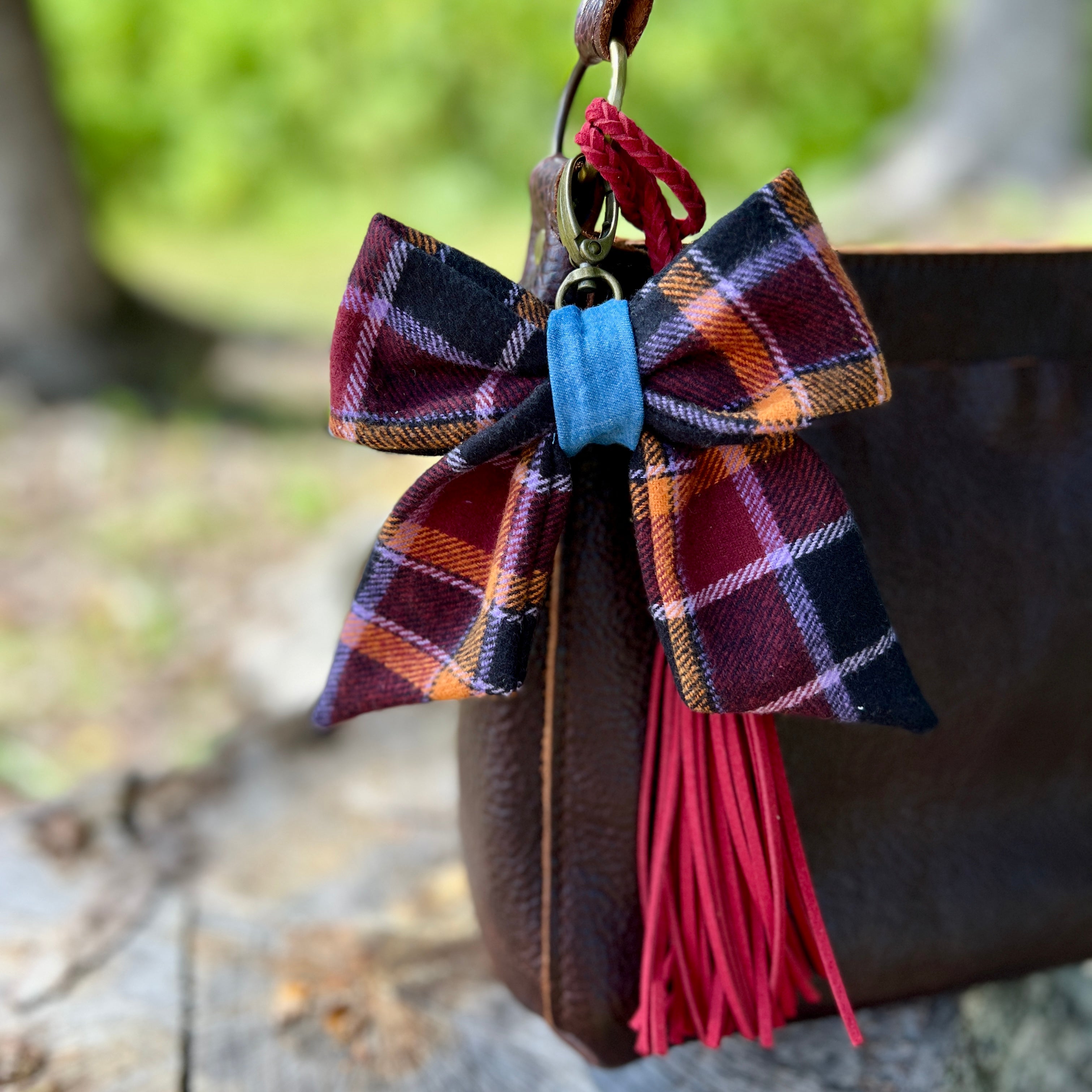 Plaid bow keychain with red tassel attached to a bag outdoors