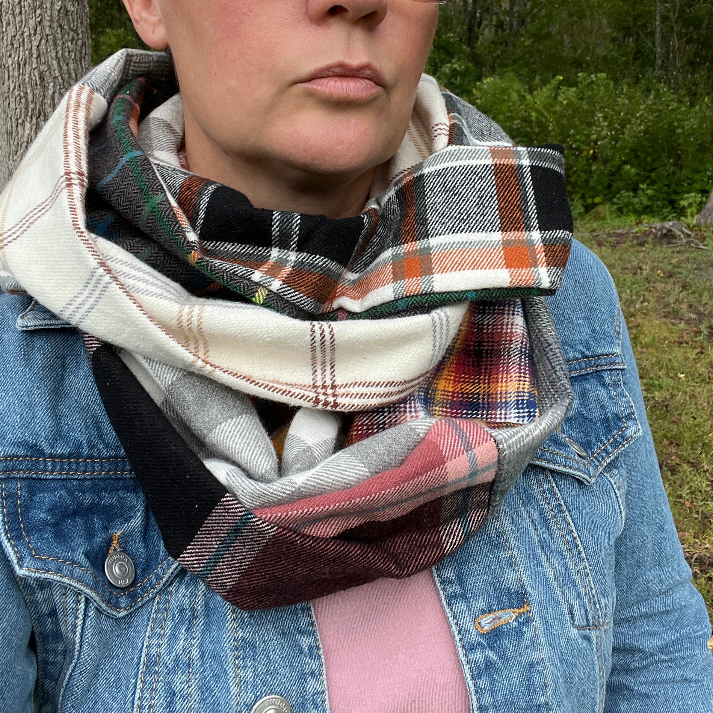 Person wearing a plaid scarf with a denim jacket outdoors