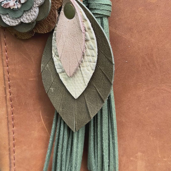 green and tan leather feather bag charm with green tassel and leather flower