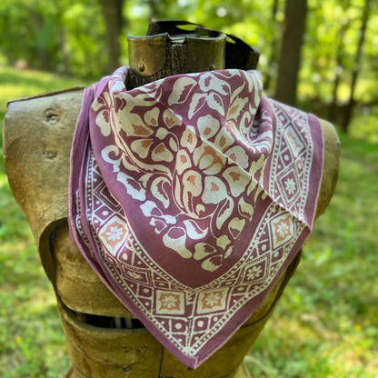 Decorative bandana with a purple and beige pattern on a wooden mannequin against a natural background.