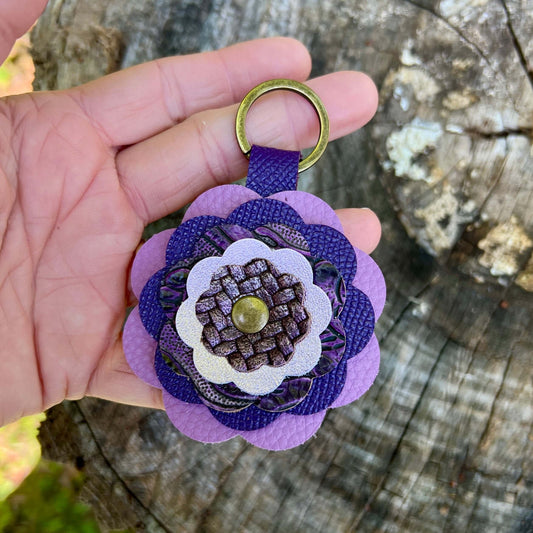 Purple leather flower bag charm held by a hand against a wooden background