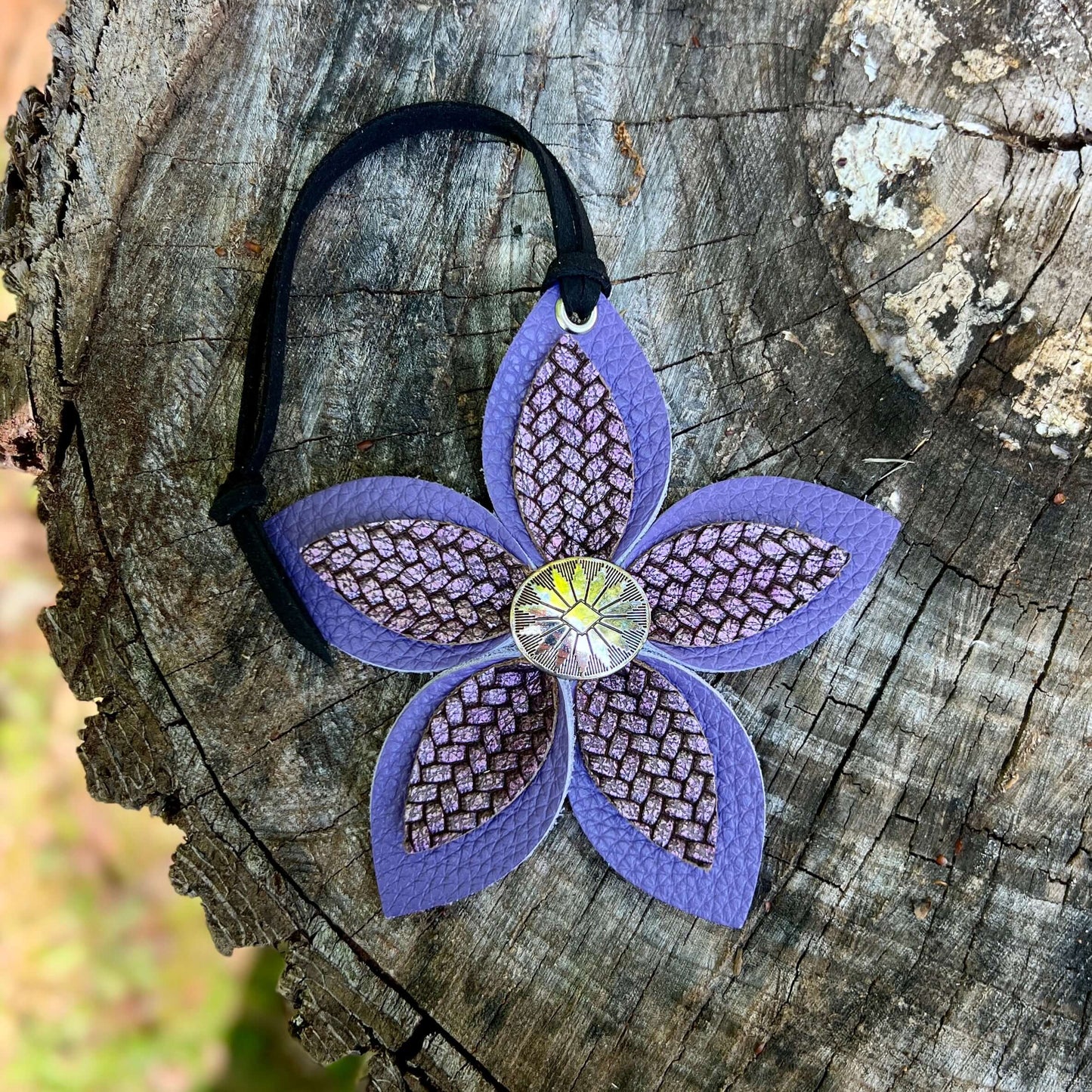 Purple leather flower bag charm with a textured center on a wooden surface