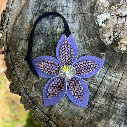 Purple leather flower bag charm with a textured center on a wooden surface