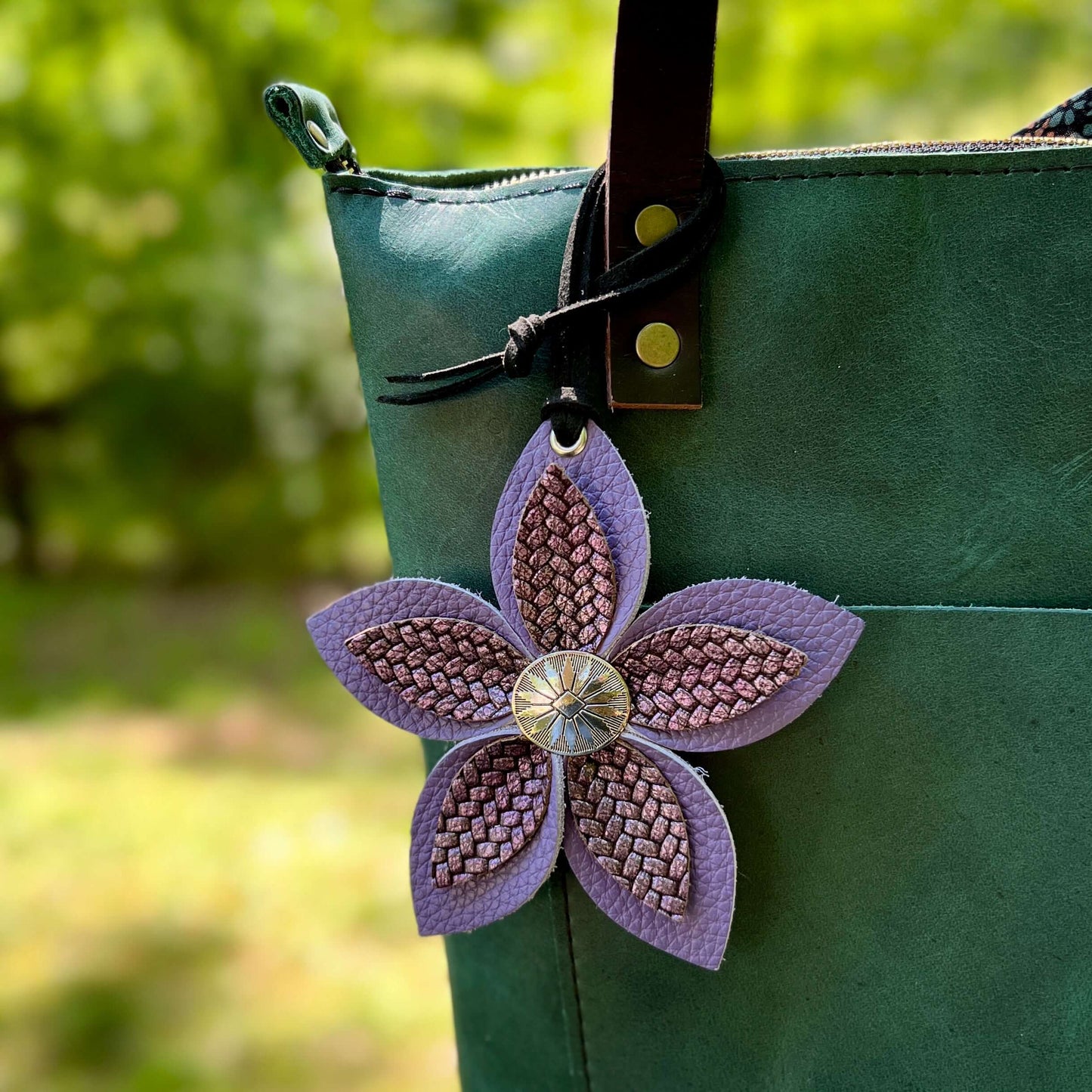 Green bag with a purple leather flower bag charm on a blurred green background