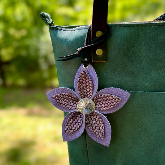 Green bag with a purple flower-shaped decorative patch on a blurred green background