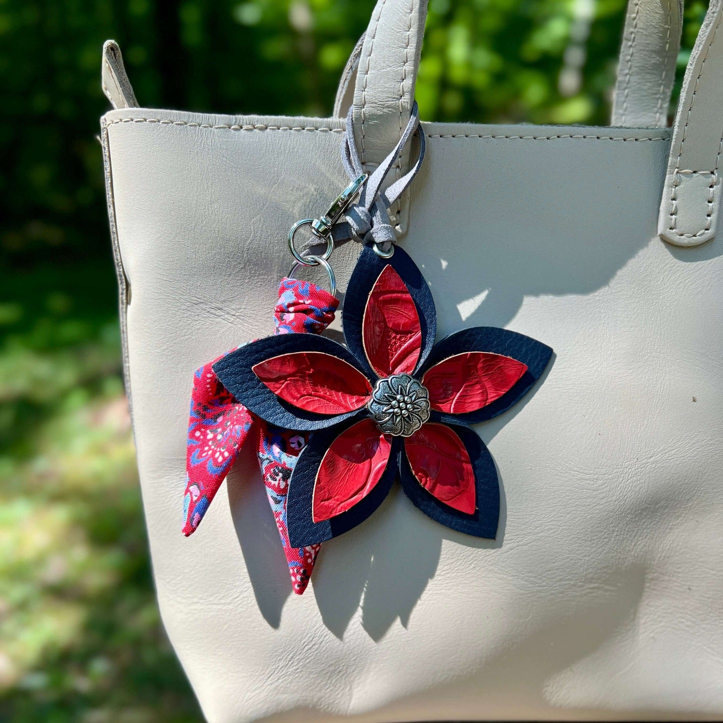 leather flower bag charm with red and blue flowers attached to a beige handbag.
