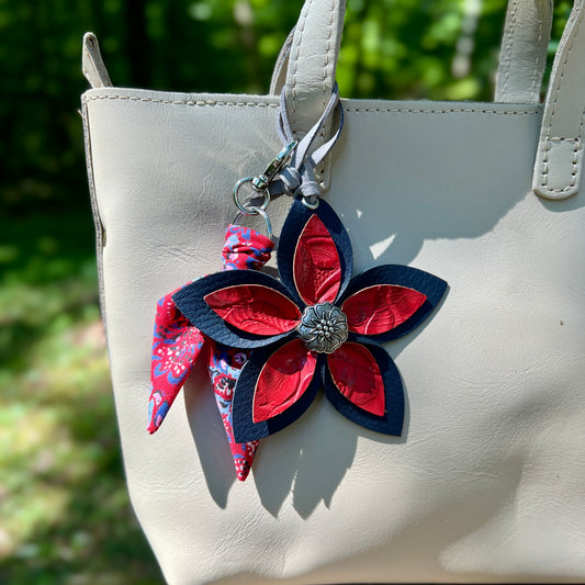 Floral keychain with red and blue flowers attached to a beige handbag.