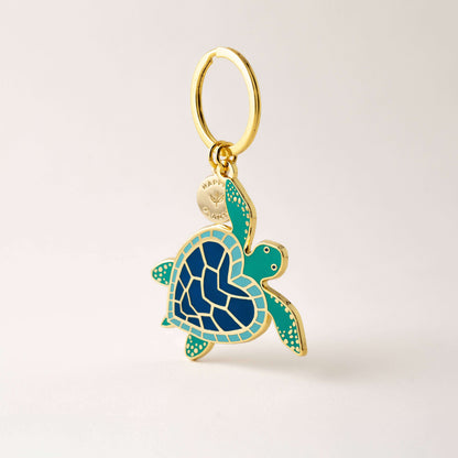 Gold and blue turtle-shaped pendant on a beige background