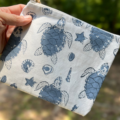 Fabric pouch with blue turtle pattern held by a hand against a blurred natural background