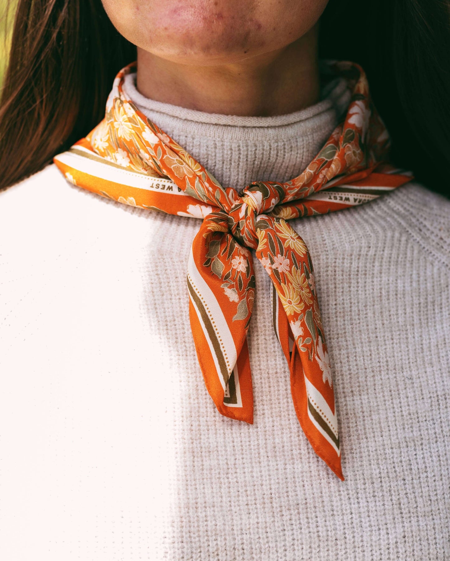 Person wearing an orange patterned scarf around their neck on a plain background