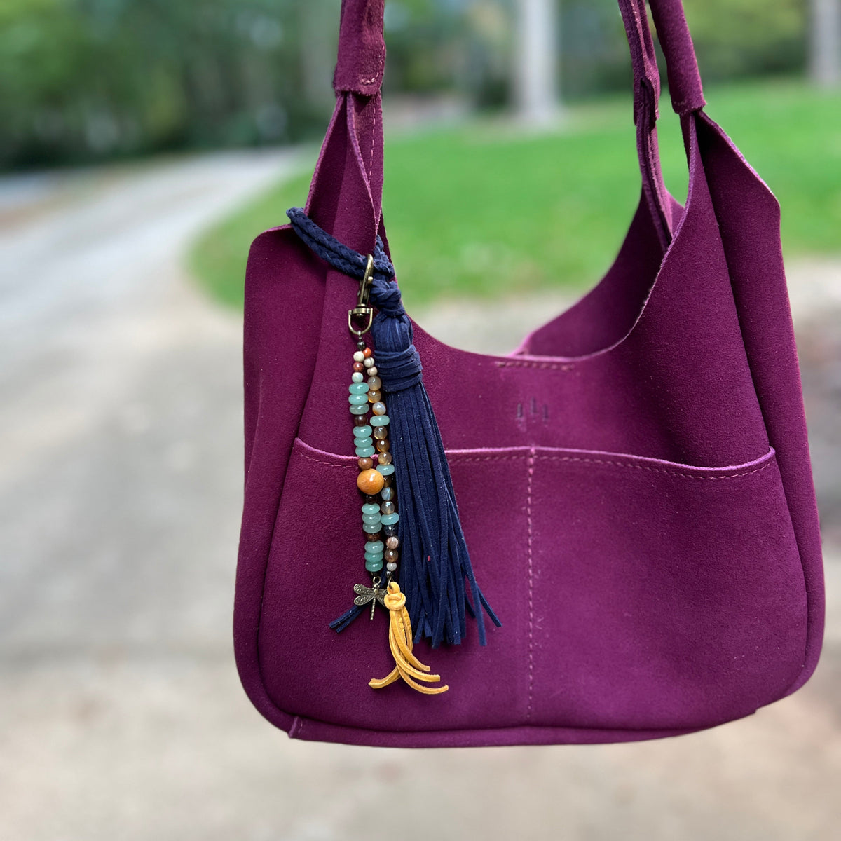 vibrant purple handbag with navy tassel and beaded bag charm with blurry background