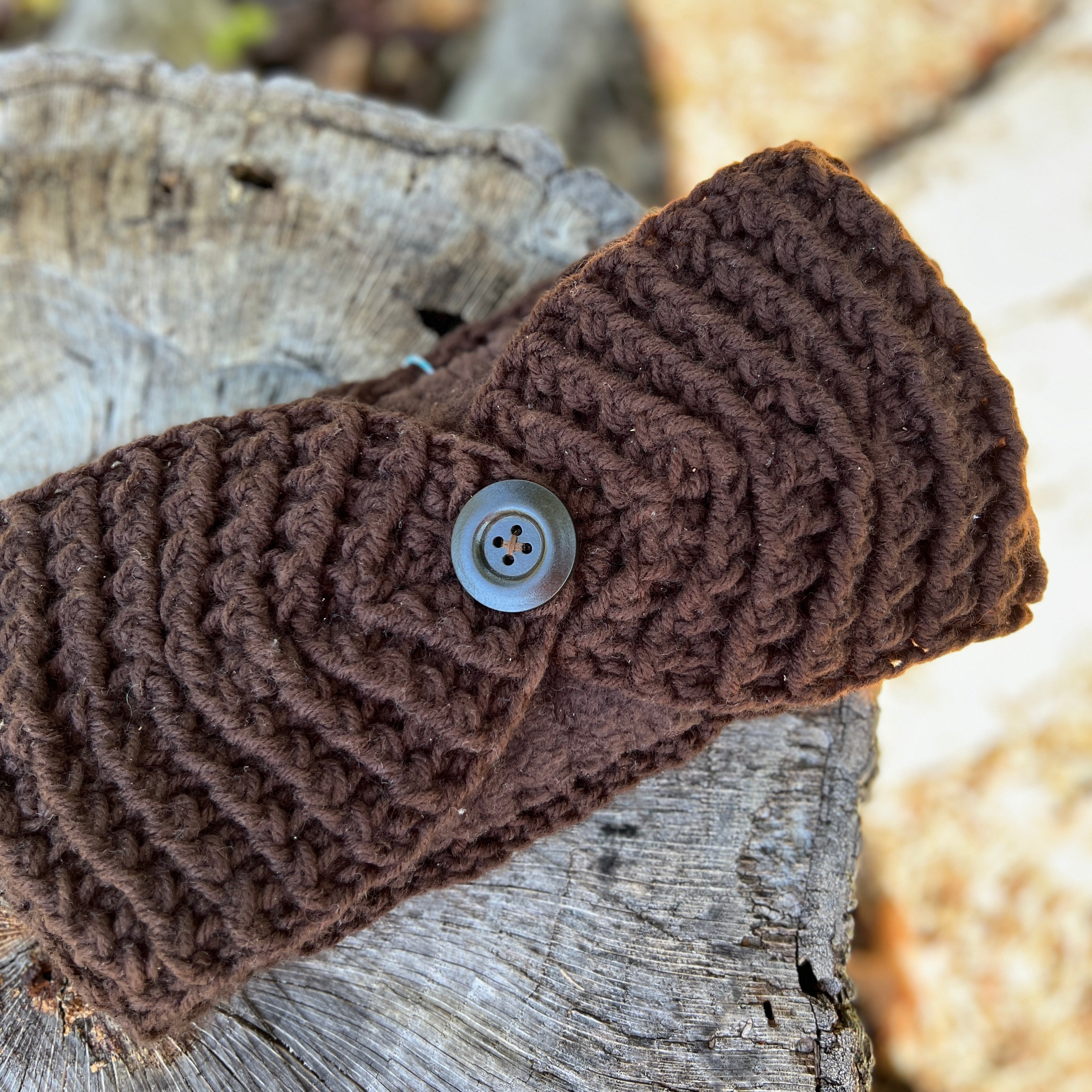Brown knitted headband with a button on a wooden surface