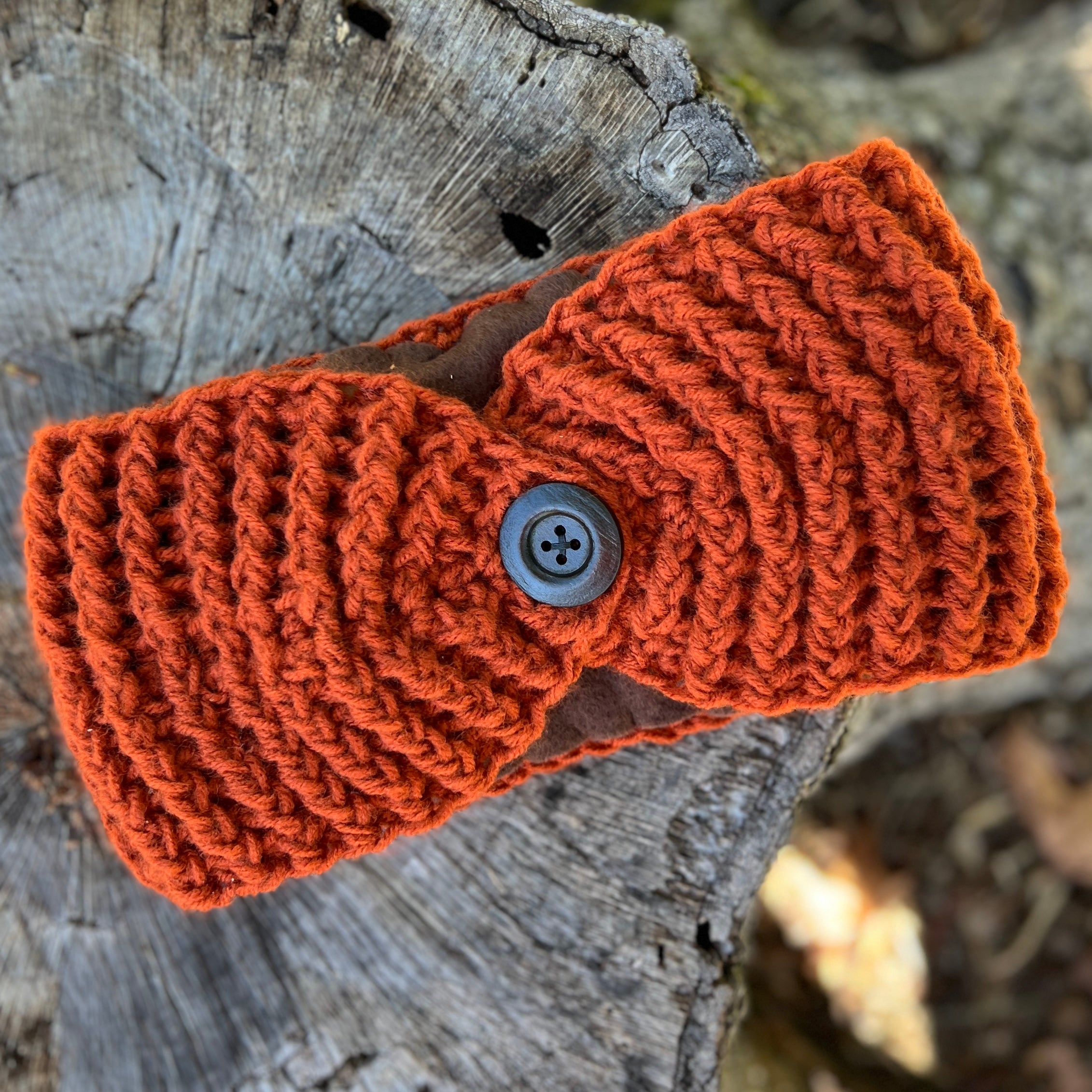 winter headband Knitted orange  with a button on a wooden surface