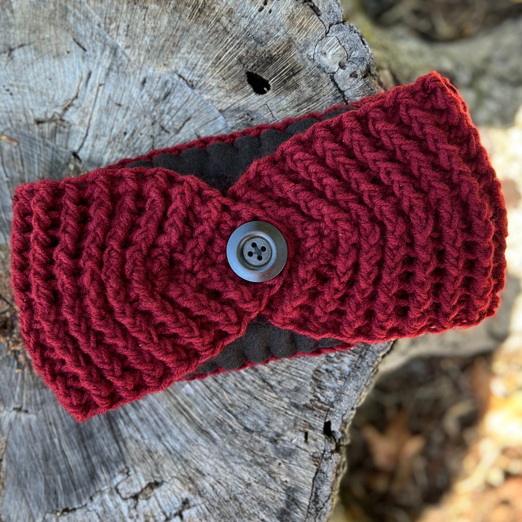 Red knitted winter headband with a button on a wooden surface