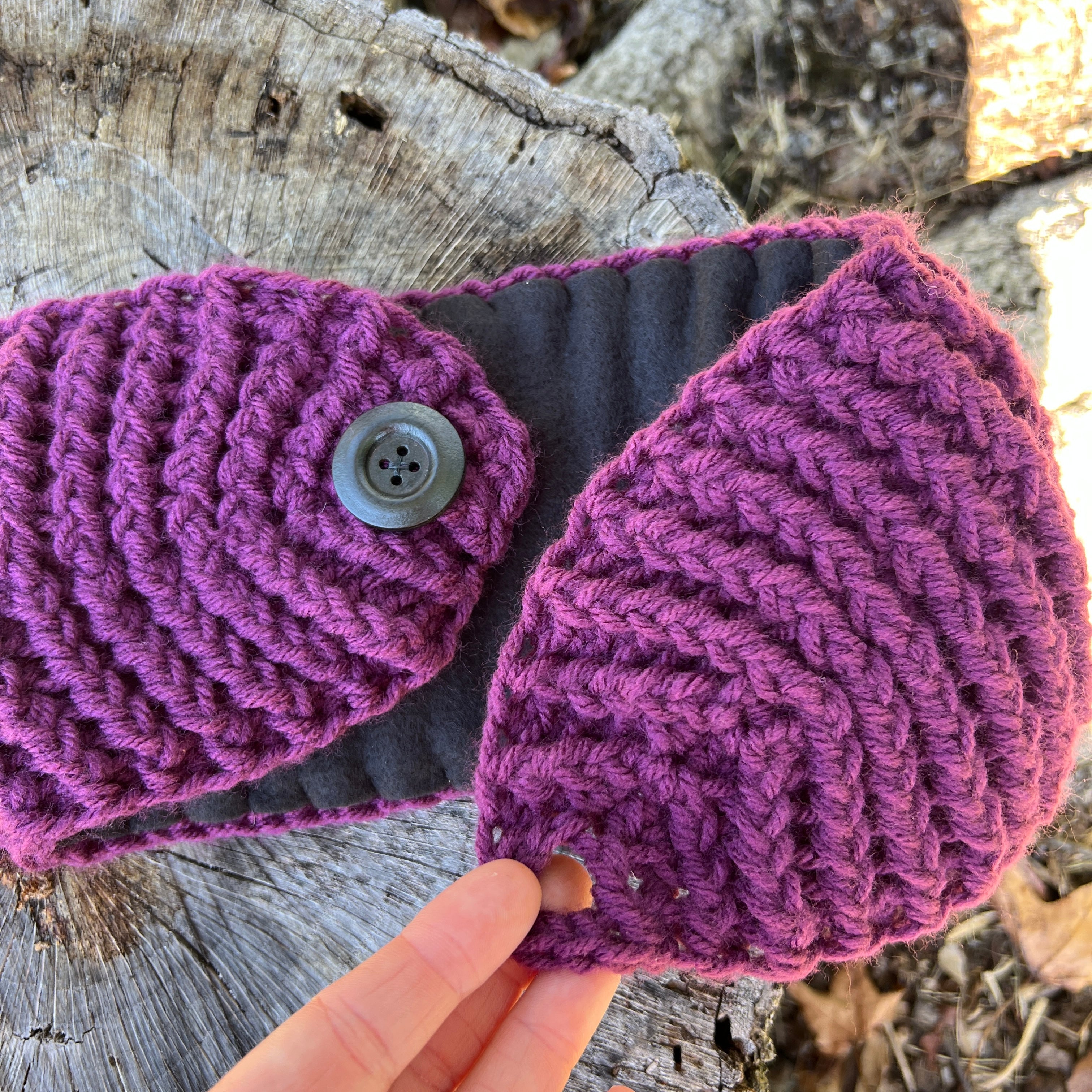 Purple knitted headband with a button held over a wooden surface