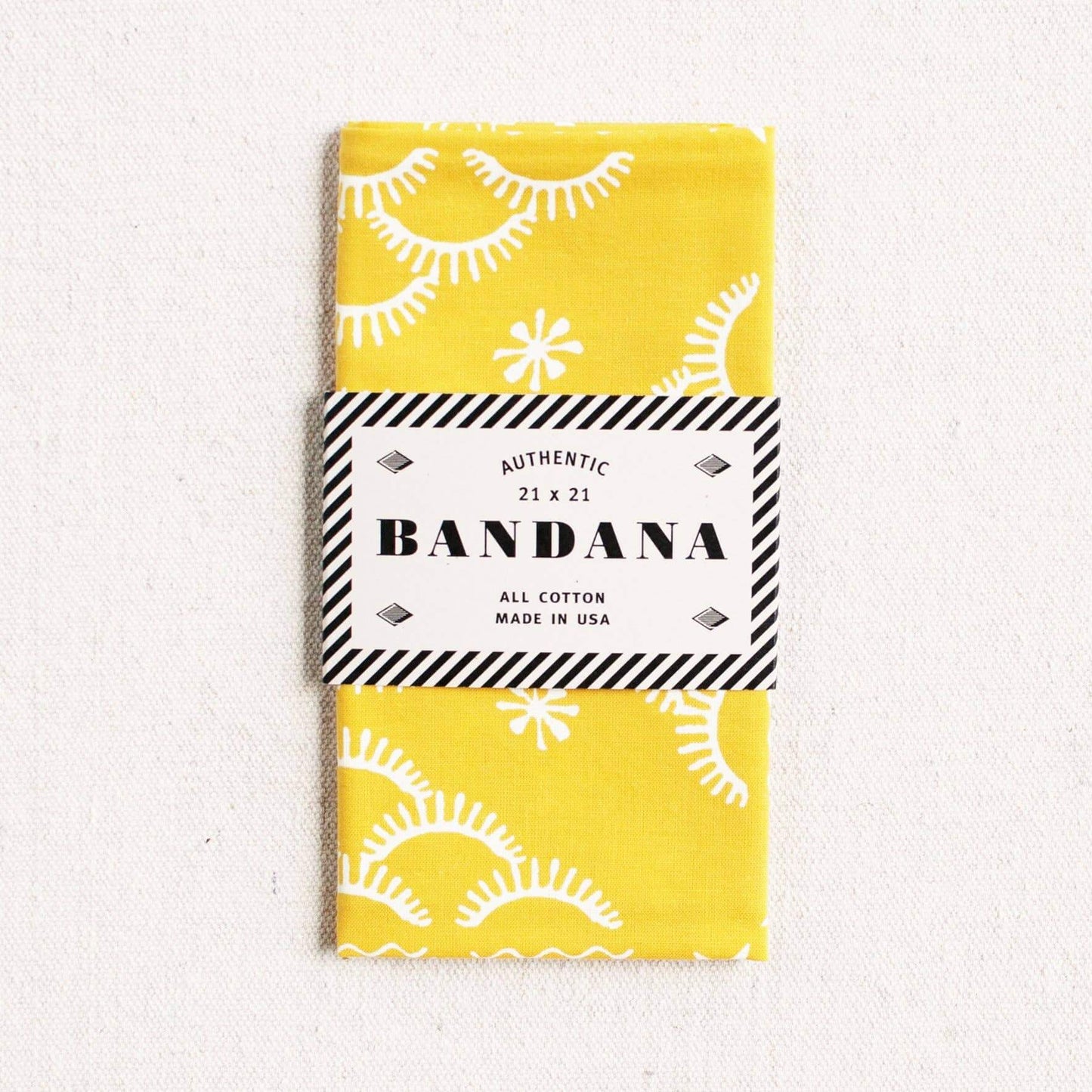 Yellow bandana with white patterns and a black and white label on a light gray background