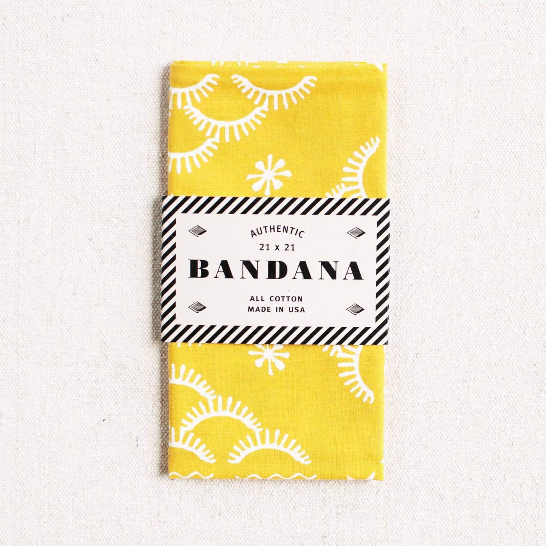 Yellow bandana with white patterns and a black and white label on a light gray background