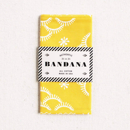 Yellow bandana with white patterns and a black and white label on a light gray background