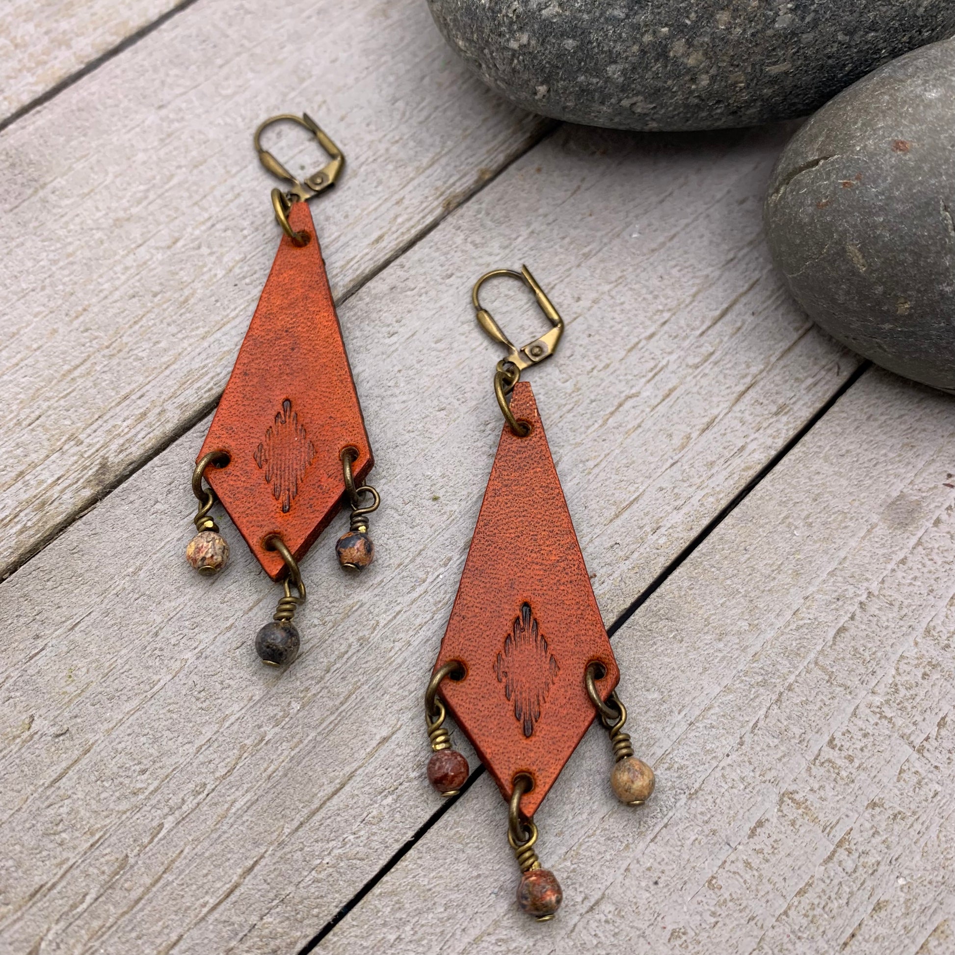 Western Style Leather Chandelier Earrings with Leopard JasperGenuine leather elongated diamond chandelier earrings. Stamped with a southwestern motif, dyed saddle tan and accented with leopard jasper dangles. Earrings dangle just under 3" long total Gold